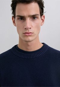 Suéter de punto texturizado azul marino con un cuello redondo acanalado. Presenta una capa interna suave debajo para mayor comodidad.