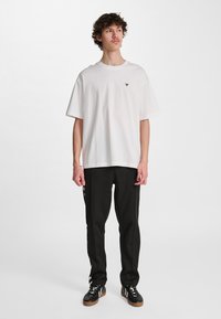 Biały bawełniany t-shirt z krótkimi rękawami i okrągłym dekoltem, z małym czarnym logo. Połączony z czarnymi dresami i trampkami.