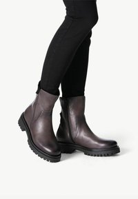 Bottines en cuir noir avec une finition lisse, fermeture éclair sur le côté et semelle à crampons en caoutchouc pour une meilleure traction ; elles présentent un léger éclat et un bout arrondi.