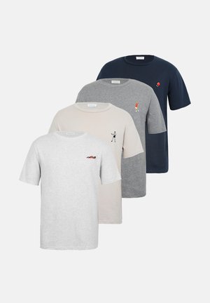 Άνδρας με τατουάζ που φοράει μπλε σκούρο t-shirt με ένα μικρό κόκκινο λογότυπο με μπαλόνι, τζιν σορτς και καφέ αθλητικά παπούτσια, στέκεται μπροστά σε απλό φόντο.