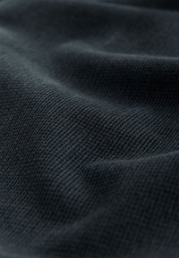 Zbliżenie ciemnej tkaniny o fakturze z wzorem dzianiny waflowej i subtelnymi fałdami tworzącymi delikatne cienie.