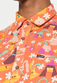 Kortærmet orange skjorte med knapper, prydet med farverige dyre- og blomstermønstre, med brune knapper og et Volcom-logo mærkat.
