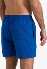 Blauwe zwembroek met een elastische tailleband, zijzakken en een achterzak met een klep en drukknoopsluiting, gemaakt van lichtgewicht stof.