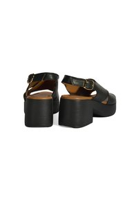 Schwarze Leder-Plateausandalen mit einem massiven Absatz, Knöchelriemen und goldfarbener Schnalle. Strukturmaterial mit einer glatten braunen Innensohle.