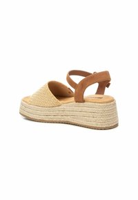 Sandal de cuña de paja tejida con una parte superior beige, acentos de ante marrón y una correa de tobillo ajustable. Presenta una suela de plataforma envuelta en yute.