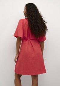 Robe corail à manches courtes en tissu texturé, avec une coupe décontractée et une ceinture à nouer à la taille, tombant juste au-dessus du genou.