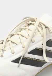 White athletic shoe with a textured surface, beige laces, and black angular accents. Designed for performance with a flexible, lightweight build.