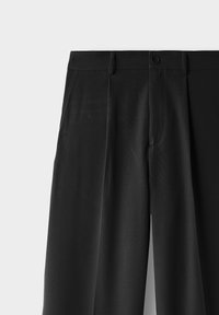 Sorte højhalset bukser med frontplisseringer, sidelommer, bæltestropper og knaplukning i taljen mod en ensfarvet baggrund.
