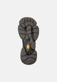 Black and grey Vibram shoe sole features a textured surface with a zigzag pattern, prominent hexagonal accents, and a yellow logo detail.