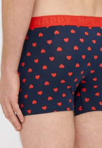 Pánske boxerky v námorníckej modrej farbe s malými červenými vzormi srdiečok. Majú červený elastický pás s nápisom "HAPPY" vyrazeným na povrchu.