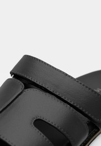 Μαύρη δερμάτινη σαγιονάρα με δύο φαρδιές ρίγες και σχέδιο κοπής. Διαθέτει λεία υφή και αντίθετο ραφές. Πλατφόρμα.