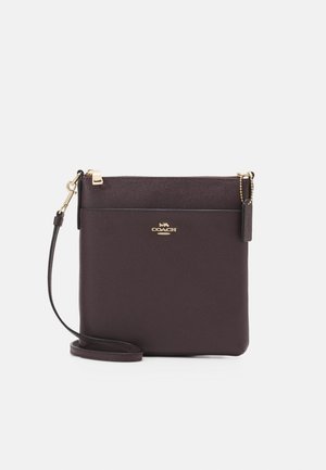 Mørkebrun læder crossbody-taske med guldlås, Coach-logo og justerbar rem mod hvid baggrund.