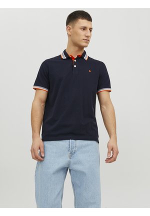 Marineblauwe polo met een kraag en manchetten in oranje en wit gestreept, met een klein logo op de borst. Draag het met lichtblauwe jeans.