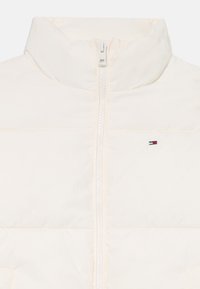 Light-colored padded vest with a high collar, front zipper, and small logo accent. Smooth texture and quilted design for insulation.