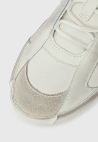 Αθλητικό παπούτσι με συνδυασμό υφασμένου λευκού δέρματος και γκρι σουέντ, στρογγυλεμένη μύτη, ραμμένα διακοσμητικά και επίπεδα κορδόνια.