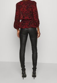 Blusa a fiori rossi con maniche a sbuffo abbinata a pantaloni attillati in pelle nera. L'outfit presenta un punto vita a peplum e una silhouette elegante.