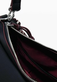 Borsa a tracolla in pelle nera con interno di un bordeaux scuro, zip in argento e dettagli in pelle decorativi. Presenta una tracolla e un'esterno testurizzato.