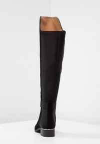 Botte noire au-dessus du genou en tissu lisse avec un design épuré, dotée d'un petit talon bloc et d'un détail en bande élastique en haut.