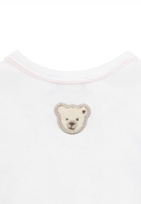 Weißes Baumwollhemd mit einer bestickten braunen Bärenkopf-Applikation auf dem Rücken, weichem Material und pastellrosa Besatz am Kragen.