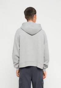 Hoodie grigio cropped realizzato in tessuto morbido, con un grande cappuccio, maniche lunghe e orlo a costine. Nessun logo o motivo visibile.