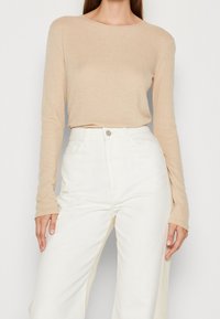Hellbeige, gerippter Langarm-Top mit rundem Halsausschnitt, kombiniert mit hoch taillierten weißen, weiten Hosen, die über Fronttaschen und einen Knopfverschluss verfügen.