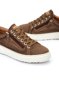 Zapatillas de ante marrón con suelas de goma blanca, que cuentan con un zip lateral, costuras a contraste y cordones marrones. Los detalles incluyen una pequeña etiqueta.