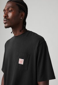 Black short-sleeve T-shirt made of cotton, featuring a chest pocket with a white tag that reads "work to be done" in red lettering.