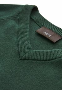 Dunkelgrüner Strickpullover mit V-Ausschnitt, ausgestattet mit einem gerippten Halsrand und einem braunen Etikett mit der Aufschrift "next". Die Textur wirkt weich.