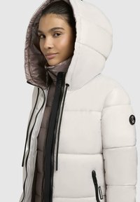 Giacca a vento con esterno bianco lucido, cappuccio oversize, zip nere e fodera beige a contrasto. Presenta il logo sulla manica.