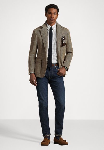Blazer marrón de espiga con solapas de muesca, camisa de cuadros clara, jeans de mezclilla oscuros, mocasines marrones y una corbata azul marino, con detalle en el bolsillo.