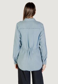 Camisa de manga larga de color azul claro, hecha de una tela suave, que presenta una cintura ajustada, puños abotonados y un dobladillo curvado.