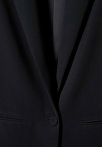 Yksirivinen musta bleiseri, jossa on lovet käänteet ja kaksi vaakasuoraa etutaskua.