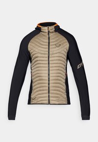 Veste isolante avec un devant beige matelassé et des panneaux extensibles noirs. Elle possède une capuche, une fermeture éclair sur le devant et des accents orange sur le col.
