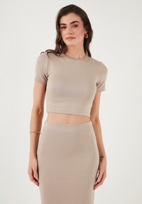 Top cropped beige realizzato in tessuto morbido, con maniche corte e scollatura rotonda, abbinato a una gonna aderente coordinata.