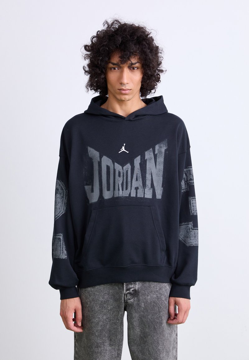 Sort hættetrøje med "JORDAN" i stort gråt tryk, og med et logo i hvid. Designet inkluderer en frontlomme og strukturerede ærmer.