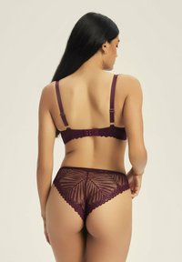 Koronkowy zestaw biustonosza i majtek w głębokim burgundzie. Biustonosz ma regulowane ramiączka i zapięcie. Majtki mają falbaniasty brzeg z geometrycznym wzorem.