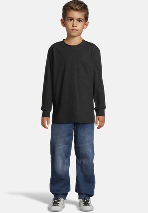 Langermet svart bomullsskjorte med brystlomme, kombinert med løse blå denimjeans med elastiske mansjetter og hvite joggesko.