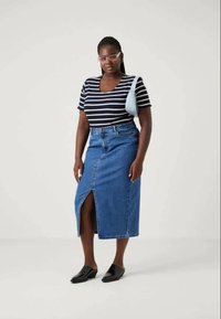 T-shirt a righe navy e bianche, gonna di jeans a vita alta con spacco frontale e scarpe nere chiuse. Borsa a spalla azzurro chiaro.