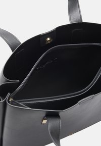 Black leather tote bag with a textured finish, designed with a spacious interior, a zip pocket, and gold hardware accents.