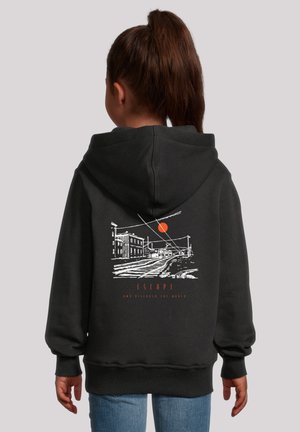 Girl with brown ponytail wearing a black hoodie featuring a white sketch of railroad tracks, buildings, and an orange sun with "ESCAPE" text.