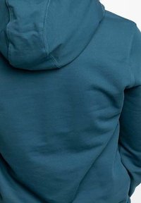 Mikina s kapucí v tyrkysové barvě, s měkkou texturou, přiléhavým střihem a viditelnými švy na zádech a kapuci.