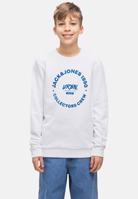 Vit sweatshirt med blå grafisk text som läser "JACK&JONES 1990" och "COLLECTORS CREW." Ribbad mudd och nederkant, avslappnad passform. Blå jeans som bärs nedan.