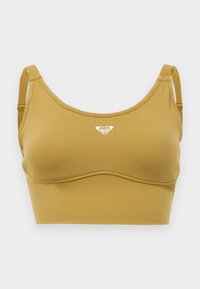 Mustard-colored sports bra made from smooth, stretchy fabric. Features a rounded neckline, adjustable straps, and a small white logo accent.