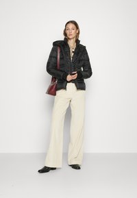 Schwarze Puffy-Jacke mit Kapuze, Reißverschluss vorne und elastischen Bündchen, kombiniert mit weit geschnittenen, hellbeigen Cordhosen und schwarzen Stiefeletten.