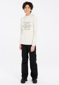 Felpa beige giovanile con testo grafico e design montano, abbinata a pantaloni da neve neri e stivali. Tessuto morbido, inclusa tasca a marsupio.