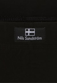 Schwarzer Stoff mit glatter Textur, versehen mit einem Etikett. Das Etikett ist weiß mit einer finnischen Flagge und dem Text "Nils Sundström."