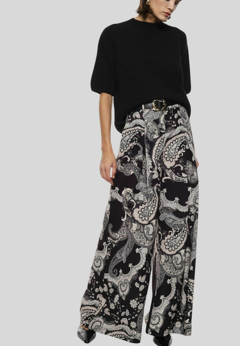 Top in maglia nera abbinato a pantaloni larghi con un motivo paisley dettagliato in tonalità di bianco e grigio. Tessuto morbido con un design fluido.