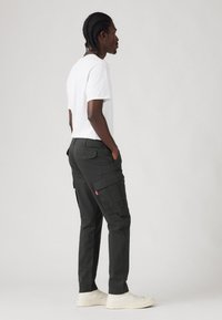 Čierne cargo nohavice s viacerými vreckami, slim fit strih a odolný materiál. Skombinované s bielou košeľou s krátkym rukávom a bielymi teniskami.