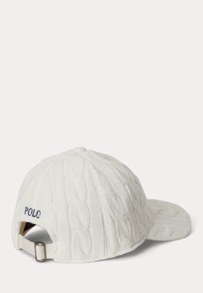 Λευκή καπέλο μπέιζμπολ με πλεκτό μοτίβο καλωδίου, με ιμάντα ρυθμιζόμενο και τη λέξη "POLO" κεντημένη σε ναυτικό μπλε στο πίσω μέρος πάνω από τον ιμάντα.