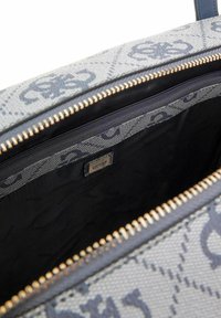 Sac à main gris à motifs avec fermeture éclair dorée. L'intérieur présente une doublure noire avec des accents de logo et un compartiment distinct. Texture lisse.